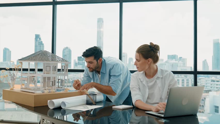 Smart architect engineer inspect house model while colleague using laptop analysis data. Professional designer team working together to design house model construction at modern office. Tracery