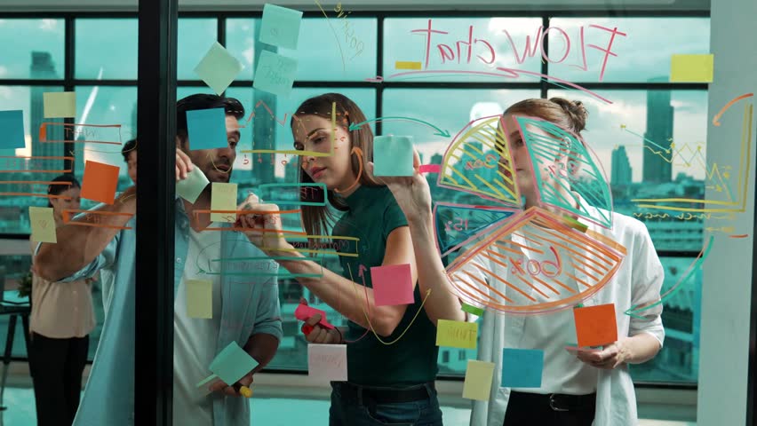 Smart business team working together to brainstorm marketing plan while putting sticky notes on glass wall with statistic graph. Group of businesspeople sharing, thinking,discussing idea. Tracery