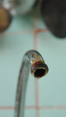 Water drops drip from rusty tap spout close up on vertical video. Increased water consumption and risk of drinking water contamination due to malfunction and poor condition of kitchen equipment.
