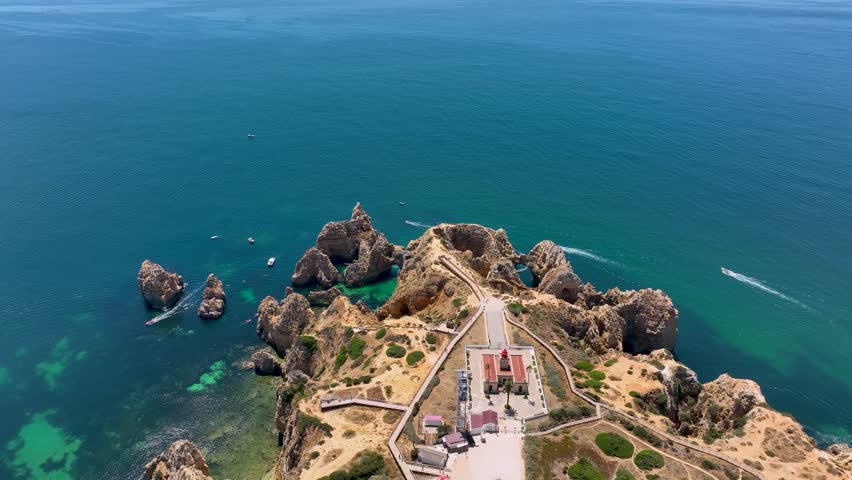 Top-down aerial view of the Ponta da Piedade lighthouse surrounded by cliffs, boats, and turquoise water in Lagos, Portugal