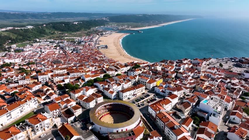 Aerial view of Nazare, Portugal, showing the red rooftops, expansive Nazare Beach, and the Atlantic Ocean along the western coastline