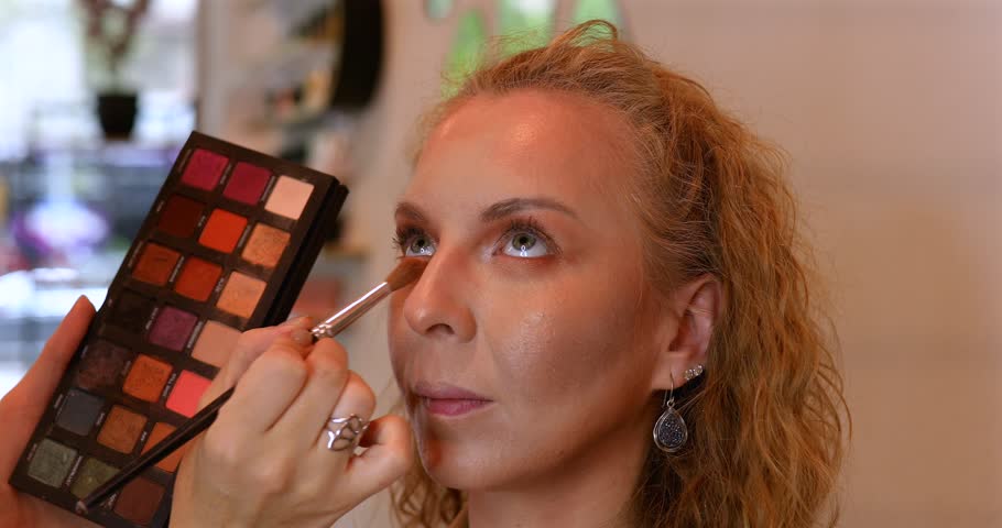 Woman is getting her makeup done by makeup artist. The woman doing the makeup is using a brush to apply it