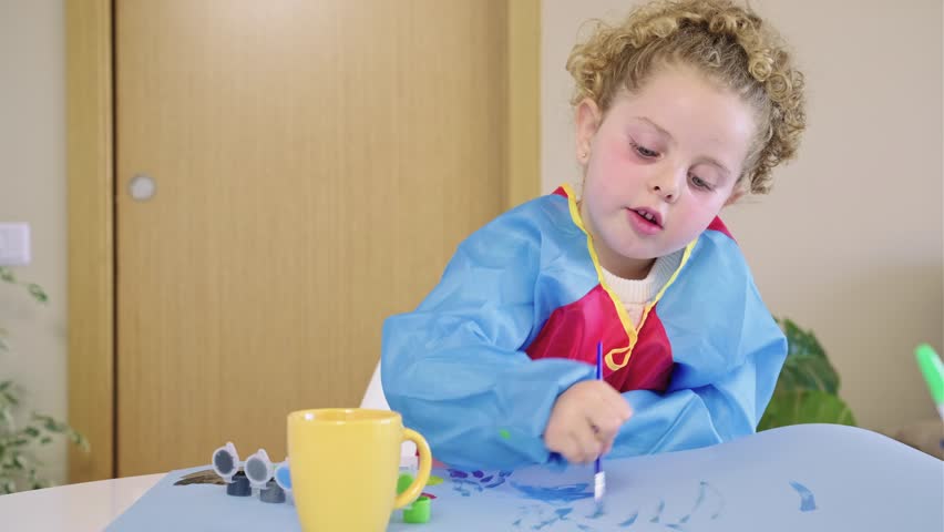 Little girl painting with tempera colors on paper sheet