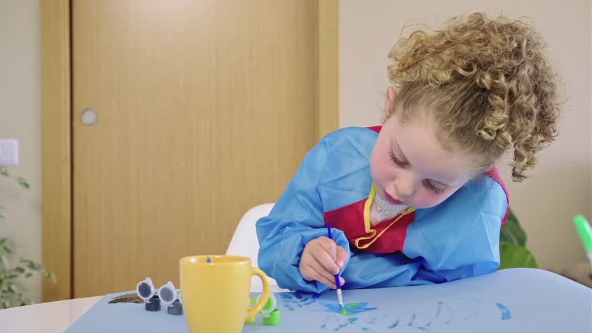 Little girl painting with tempera colors on paper sheet