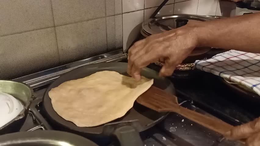 hands expertly making roti on a frying pan. Watch the step-by-step process of cooking traditional Indian flatbread on a stovetop, featuring dough rolling, flipping, and puffing techniques. Ideal for f