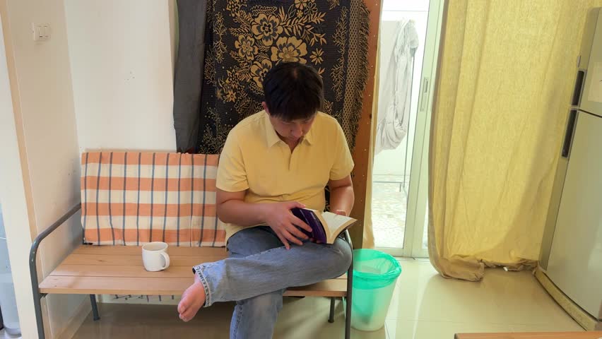 The East Asian man is reading a book at home.