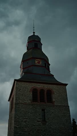 Thunder and lightning in the cloudy evening sky, Over the Protestant Church. Upward view of an old clock tower under a moody, cloudy sky, showcasing historical architecture and timeless beauty. 
