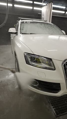 White car being pressure washed at indoor car wash, front view of vehicle during foam cleaning process