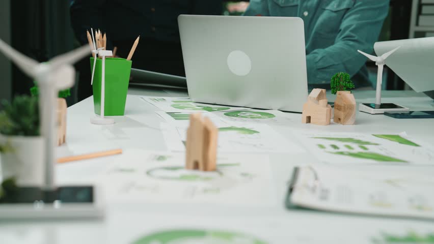 A group of professionals discussing sustainable development strategies while analyzing renewable energy models and green technology reports in a collaborative office environment. SACTR