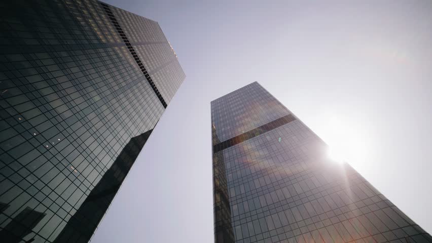 Two high-rise buildings are illuminated by the rays of the sun against the blue sky. Urban business atmosphere in the frame