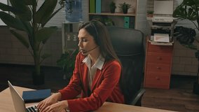 Daily lifestyle concept. Older adult businesswoman works at green office with plants, woman sitting at desk working on laptop, typing on keyboard and talking in headset. - Powered by Shutterstock - Get 15% off with code: PIKWIZARD15