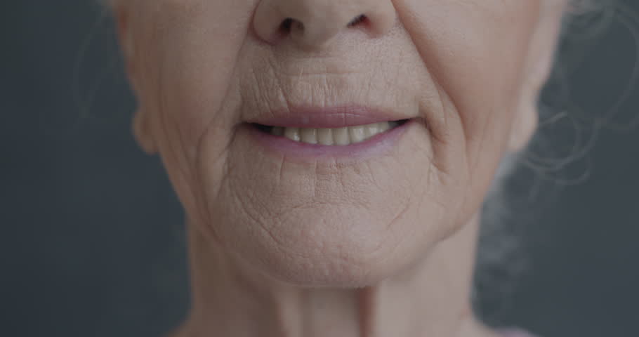 Close-up slow motion portrait of senior woman's mouth smiling on black color background. Old age and positive emotion concept.