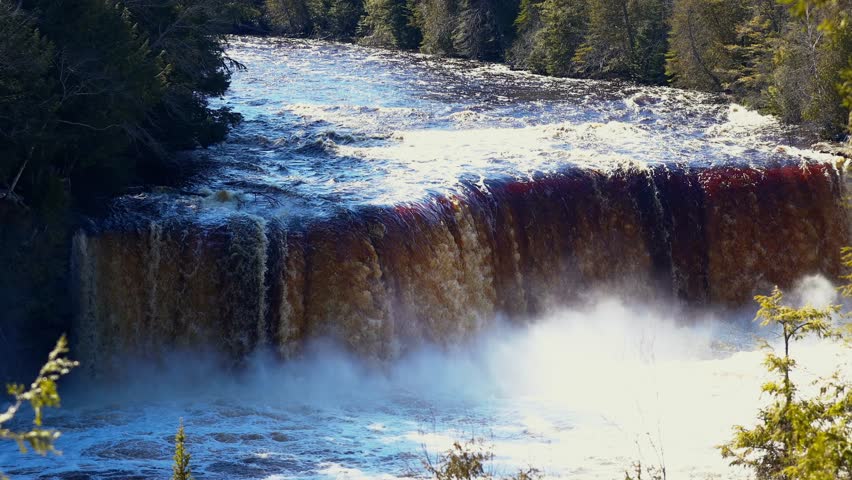 Upper Falls at Tahquamenon Falls State Park in Michigan on a sunny day with cascading water and lush green forest.