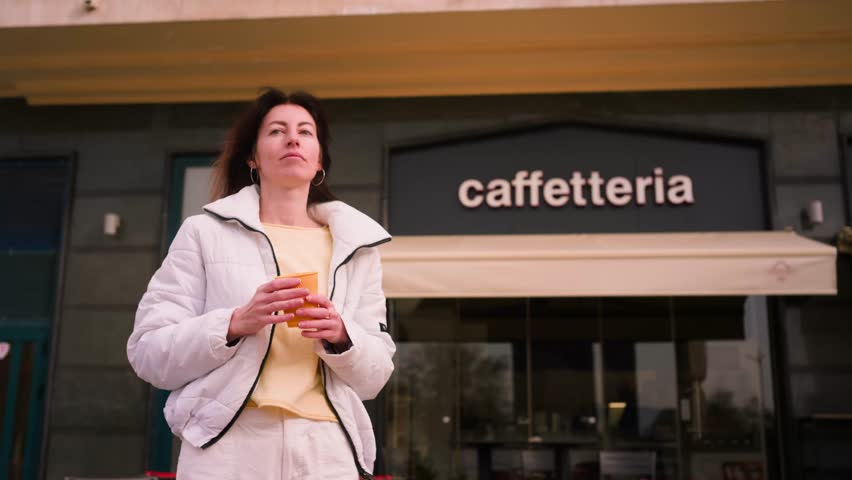 Young female drinking coffee from yellow paper cup behing coffee shop