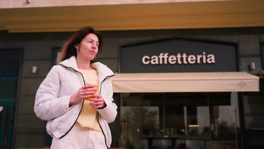 Young female drinking coffee from yellow paper cup behing coffee shop