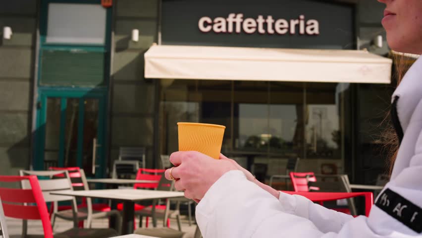Young female drinking coffee from yellow paper cup behing coffee shop