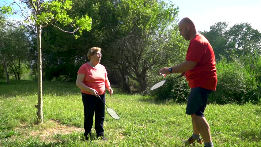  A man with his retired mother playing rackets in the park.