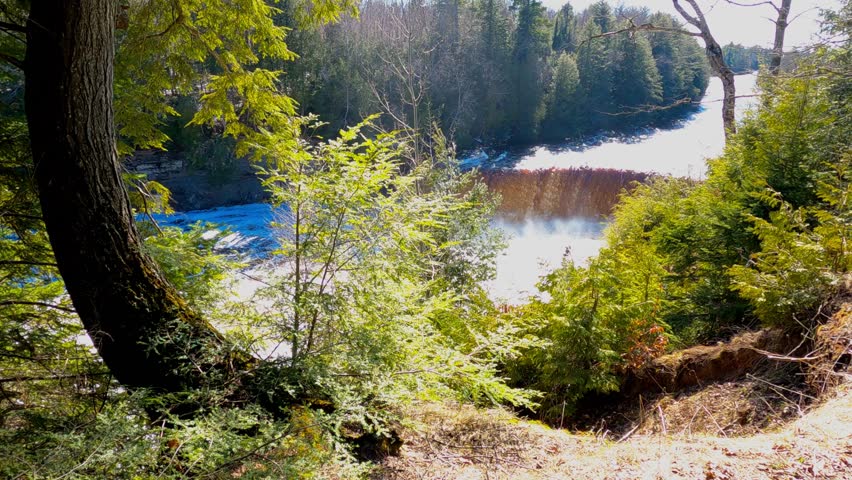 Upper Falls at Tahquamenon Falls State Park in Michigan on a sunny day with cascading water and lush green forest.