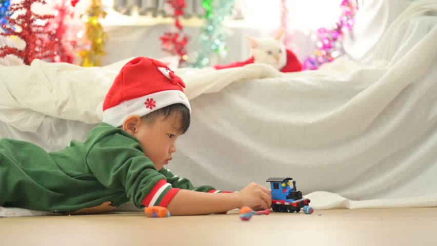 Joyful Christmas Morning: A young child, adorned in a festive Santa hat and Christmas themed attire, immerses themselves in the pure joy of opening gifts near a beautifully adorned Christmas tree.