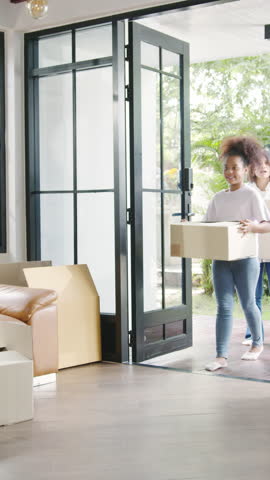 Vertical Screen : Happy African American young family bought new house. Mom, Dad, and child smiling happy hold cardboard boxes for move object walking into big modern home. New real estate dwelling.