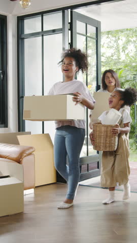 Vertical Screen : Happy African American young family bought new house. Mom, Dad, and child smiling happy hold cardboard boxes for move object walking into big modern home. New real estate dwelling.