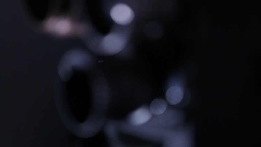 Close-up: vintage movie camera lens turret. Rack focus reveals a tangled pile of unspooled film strip in the dimly lit background. Evokes nostalgia, analog filmmaking.