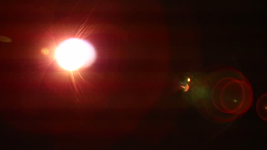 Close-up of a movie projector lens emitting bright, flickering light. Intense red and blue lens flares illuminate dust particles as abstract images project through the lens.