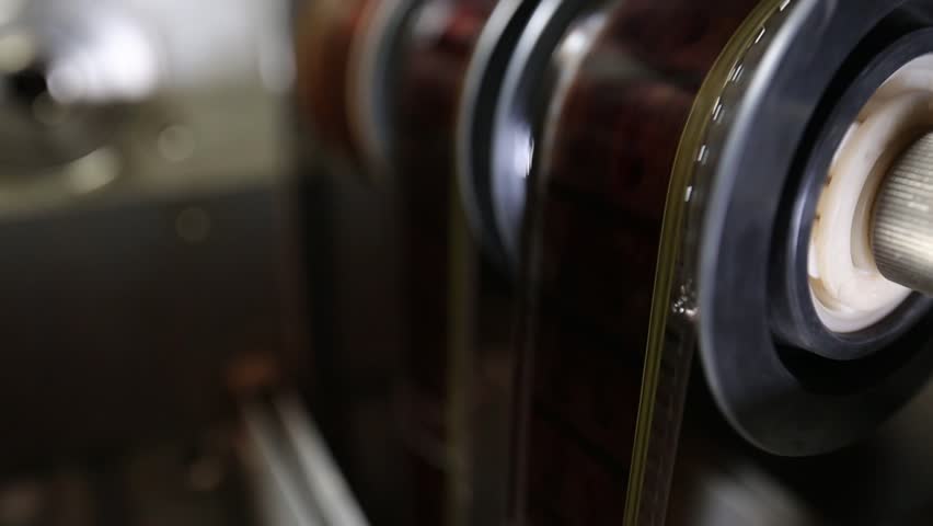  Macro shot: Vintage film strips glide through intricate projector or scanner rollers. Evokes cinema nostalgia and analog processes. Perfect for archival, retro, or filmmaking themes.