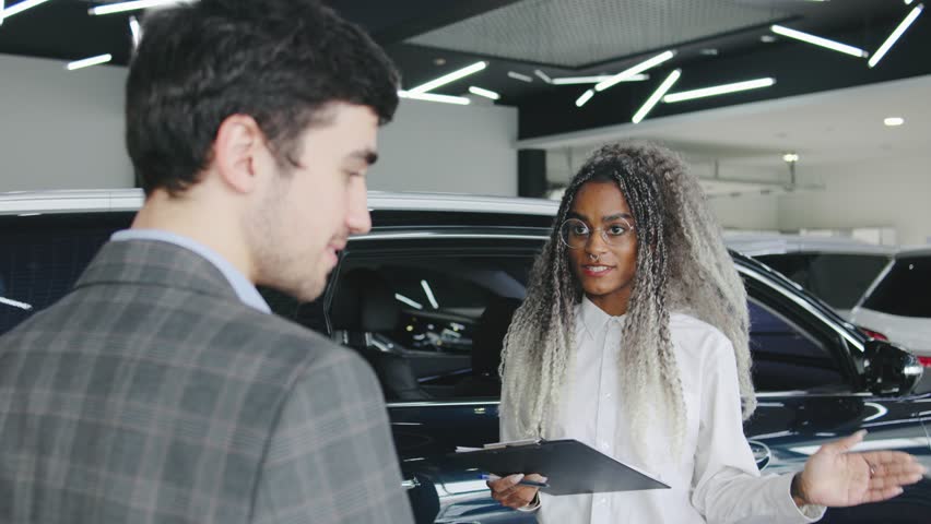 Young man interacts with salesperson in car dealership, discussing vehicle options and features during showroom visit