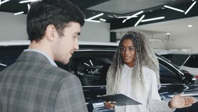 Young man interacts with salesperson in car dealership, discussing vehicle options and features during showroom visit - Powered by Shutterstock - Get 15% off with code: PIKWIZARD15