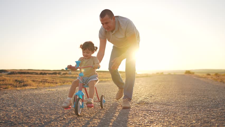 Father teaches his daughter how to ride a bike. Family childhood girl concept. Father and child playing with a bicycle. A father teaches his daughter how to ride a lifestyle bicycle.