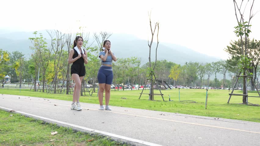 Two Asian women having fun exercising, jogging, stretching or working out together in a park in the evening.