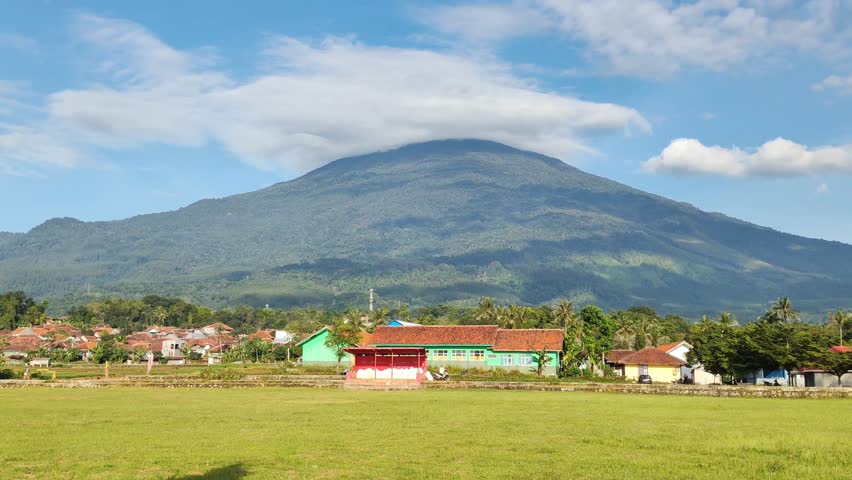 Landscape view on a bright morning, football field, with Mount Ciremai and local houses in the background