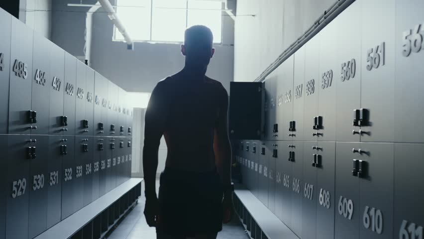 A silhouette of a male athlete standing in a gym with strong backlighting that highlights the industrial interior. The scene conveys determination and strength. Silhouetted Athlete in Gym