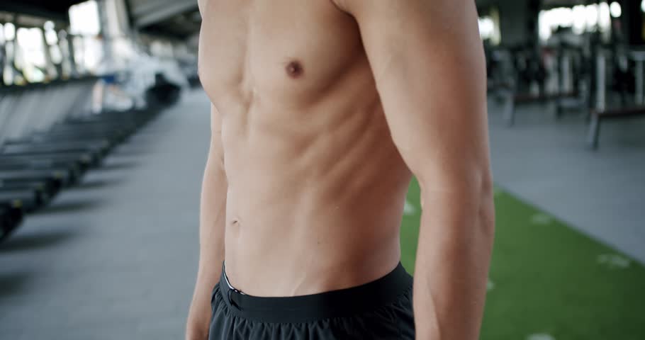 A close-up image of a fit young man's torso, displaying his muscular abs in a gym setting, evoking themes of fitness, health, and dedication. Fit Young Man in Gym Showing Off Muscular Torso and Abs