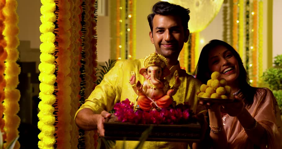 Indian Couple Welcoming Ganesh Idol with Joy, Young husband wife in Traditional Attire Holding Ganpati Bappa Idol, laddu thali While Smiling Chanting Bappa Morya During Ganesh Festival Celebration