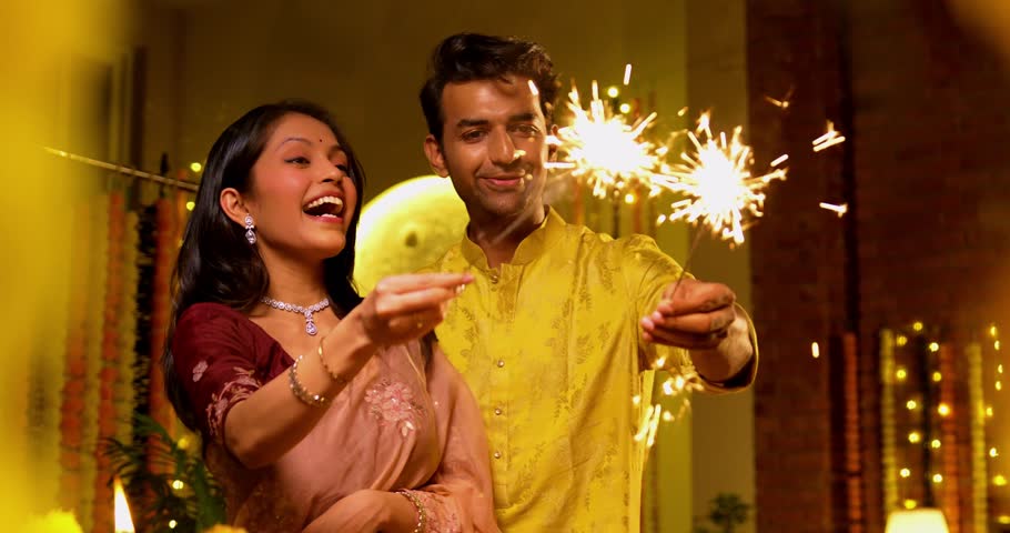 Indian Couple Lighting Sparklers Together While standing near railing in Traditional Festive Attire, Smiling and Celebrating Joyfully During Diwali Night with Sparkles and Firecrackers