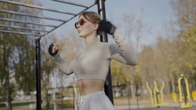 A fit young woman with sunglasses performs boxing exercises in a park surrounded by autumn trees, conveying energy and health. Young Woman Exercising Outdoors on a Sunny Autumn Day - Powered by Shutterstock - Get 15% off with code: PIKWIZARD15