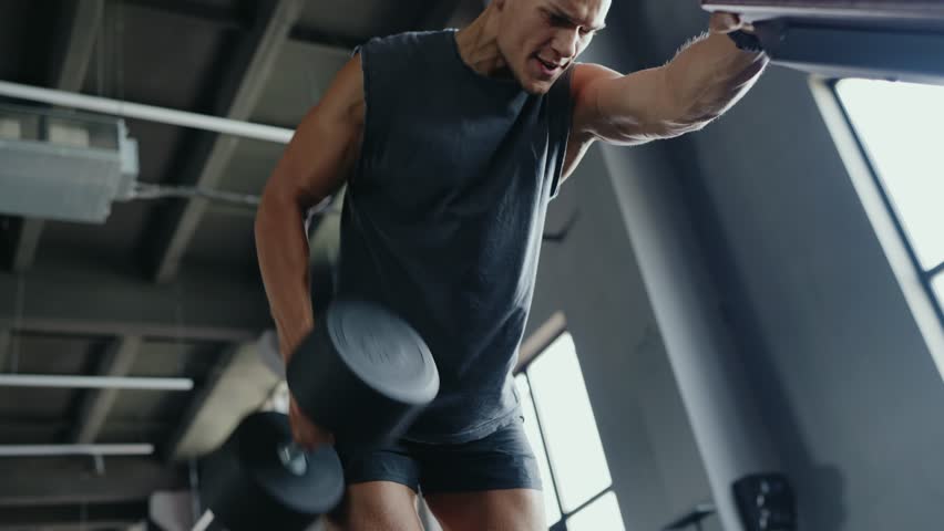 Man working out intensely in an industrial-style gym. He is exerting effort, showcasing determination and physical strength during his fitness routine.