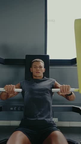 Athletic man working out on a chest press machine in the gym. He is focused and determined. Focused Man Exercising on Chest Press Machine at the Gym. Man Exercising on Machine in Gym. Vertical