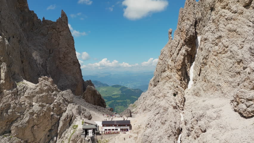 Backwards reveal drone shot of the iconic Toni Demetz Hut perched dramatically in the Forcella del Sassolungo, Dolomites, Italy