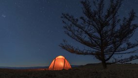 Timelapse of camp with orange illuminated tent near tree at night and moonset - Powered by Shutterstock - Get 15% off with code: PIKWIZARD15