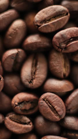 Closeup shot of a pile of roasted coffee beans rotating under bright natural light