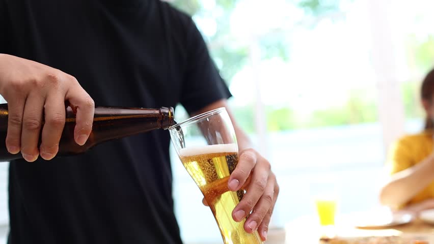 A young bartender pours a fresh beer into a glass at a shiny metal bar, capturing motion, craftsmanship, and the energy of a modern pub setting.
