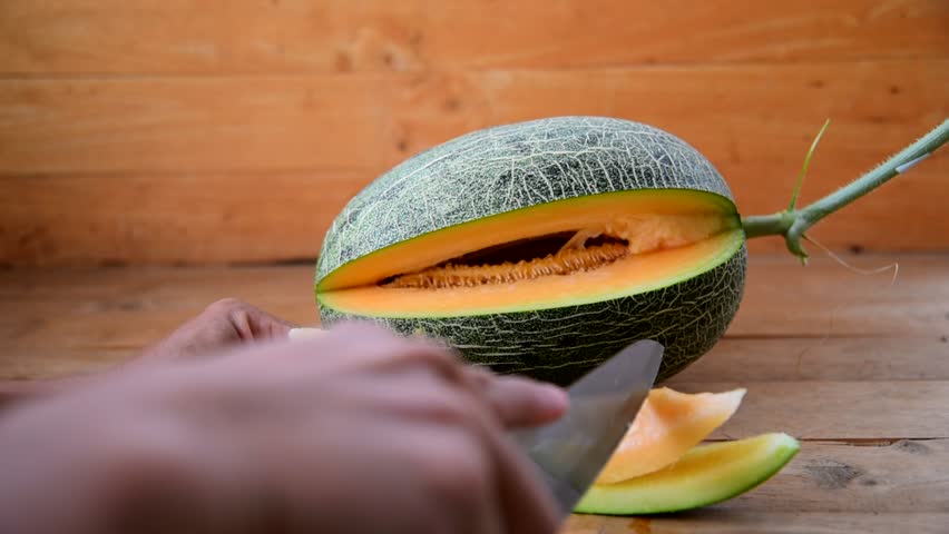 The man use knife split the orange melon on wood plate