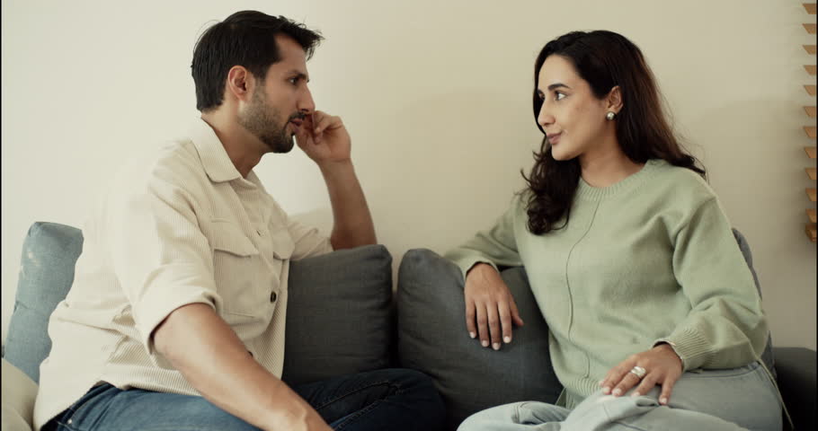 Husband and wife having a serious conversation on the sofa. Concept of communication, emotional relationship, family issues, or personal discussion in modern cozy home.