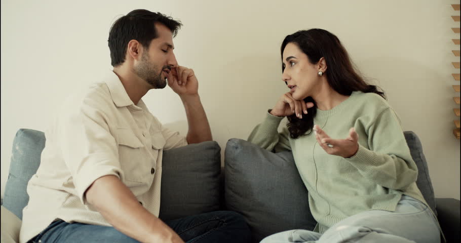 Husband and wife having a serious conversation on the sofa. Concept of communication, emotional relationship, family issues, or personal discussion in modern cozy home.