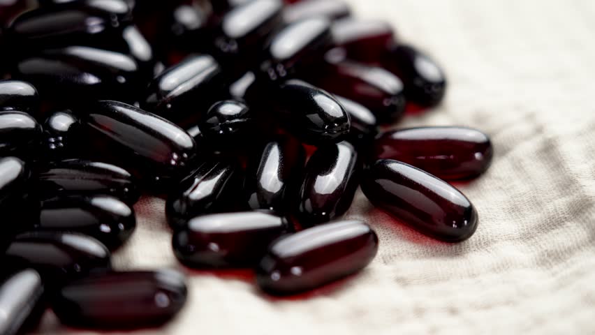Dark red translucent softgel capsules of Omega 3 supplement on a soft cloth napkin close-up. Rotation
