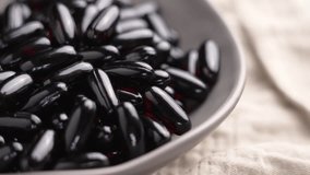 Black red soft gel Omega 3 capsules falling into bowl on crumpled tablecloth in slow motion close up. Nutritional supplements - Powered by Shutterstock - Get 15% off with code: PIKWIZARD15