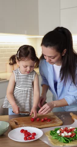 cute toddler child girl with mother making a pizza at home kitchen
